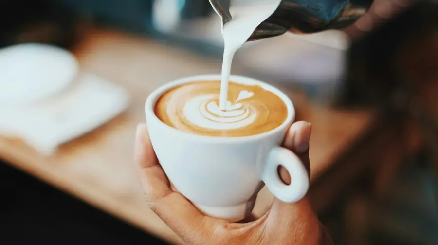 Hand die een hartje van melkschuim in een cappuccino giet